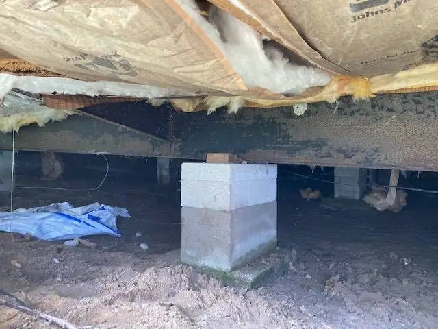 Bare soil and a block pier under a manufactured home before a ground barrier