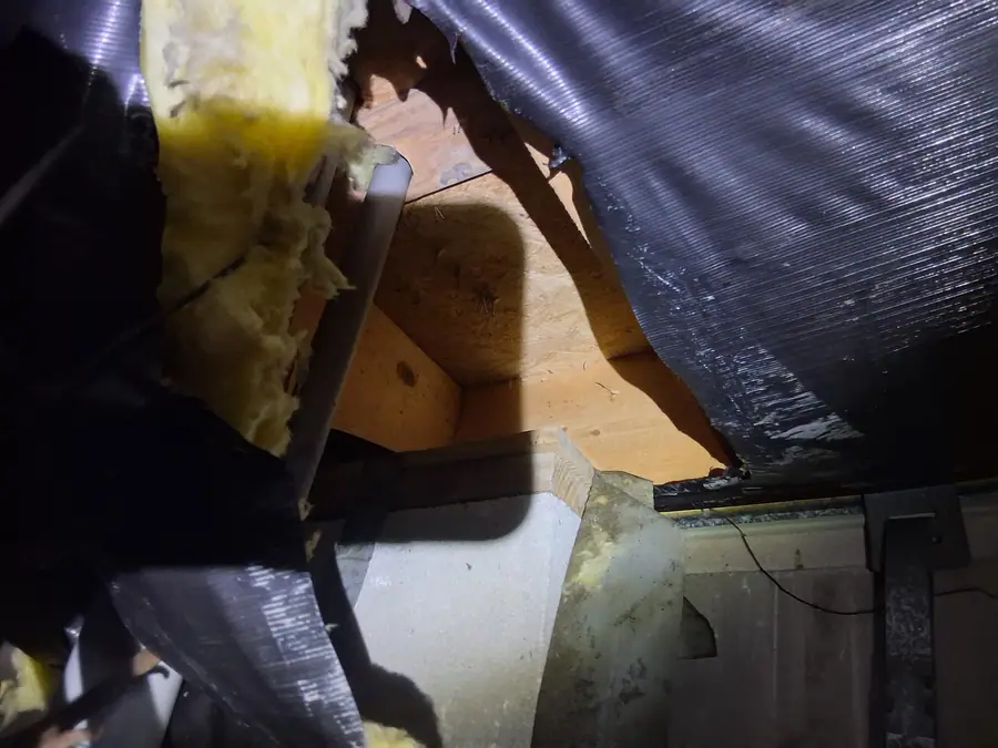 Torn belly wrap opened beside a pier, yellow insulation and framing showing