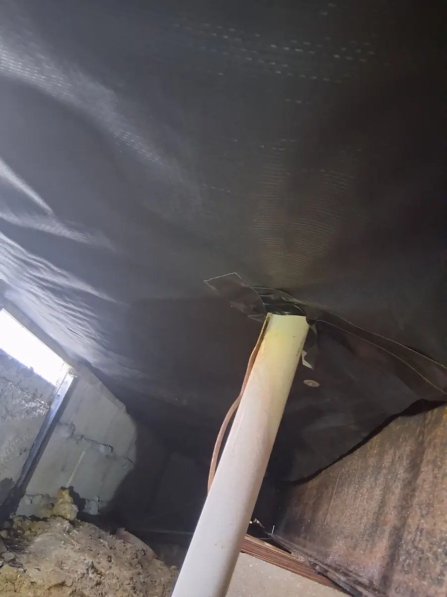 PVC drain pipe passing through black belly wrap above a block pier