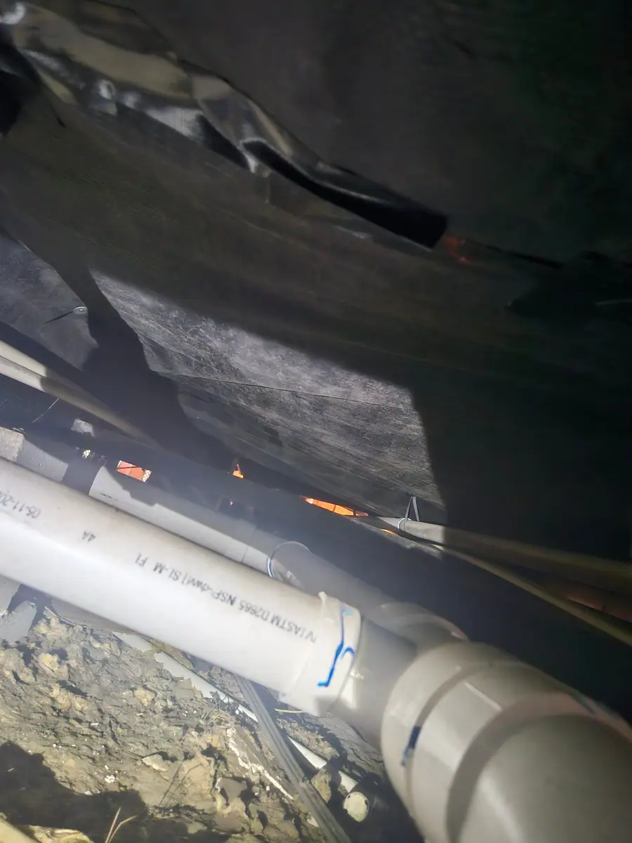 White PVC drain line running under torn black belly wrap
