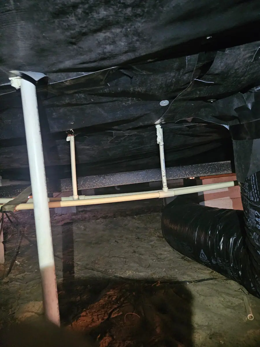 PVC pipe hanging from black belly wrap beside a flex duct