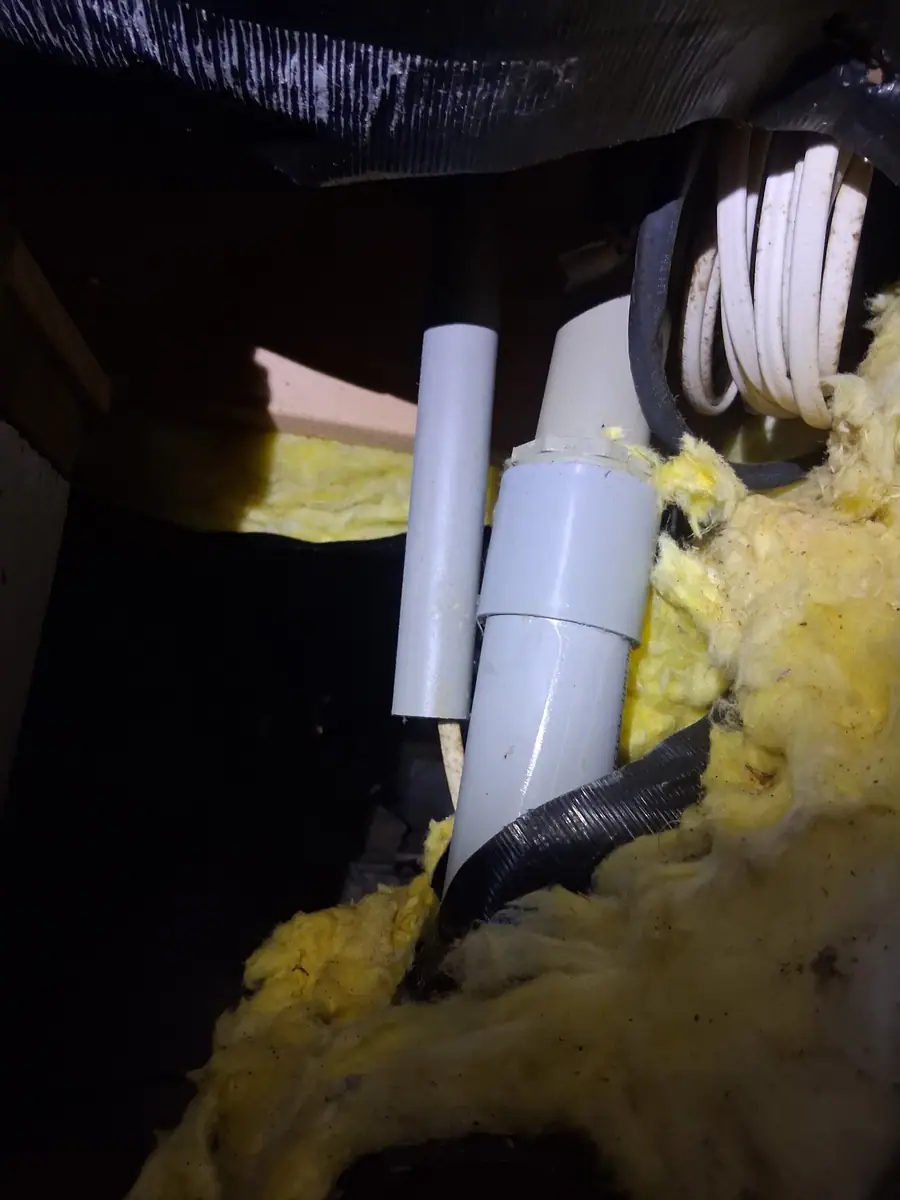 Yellow fiberglass insulation hanging down around plumbing under a torn belly