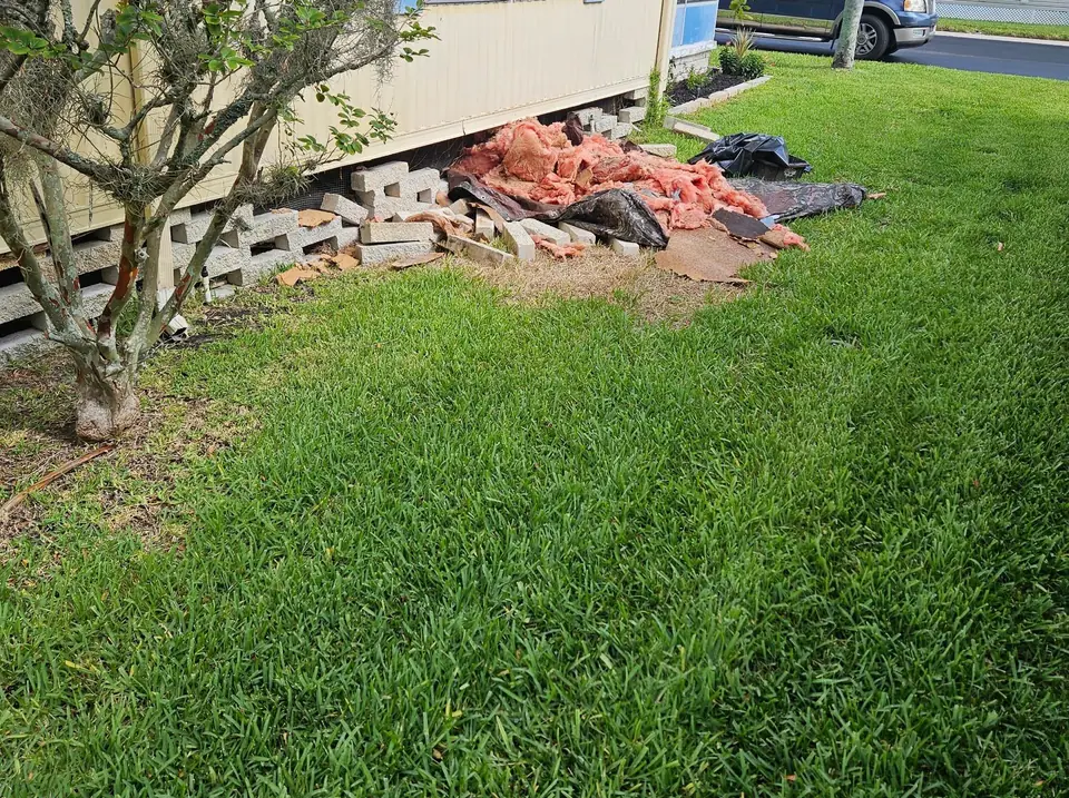 A manufactured home on block piers with old material piled on the lawn during a job