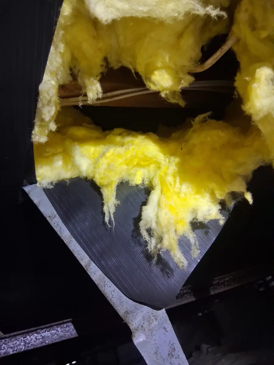 Torn belly board under a mobile home with fiberglass insulation falling out of the hole