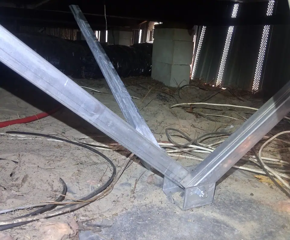 Galvanized V-strut stabilizers set on a ground pan under a manufactured home