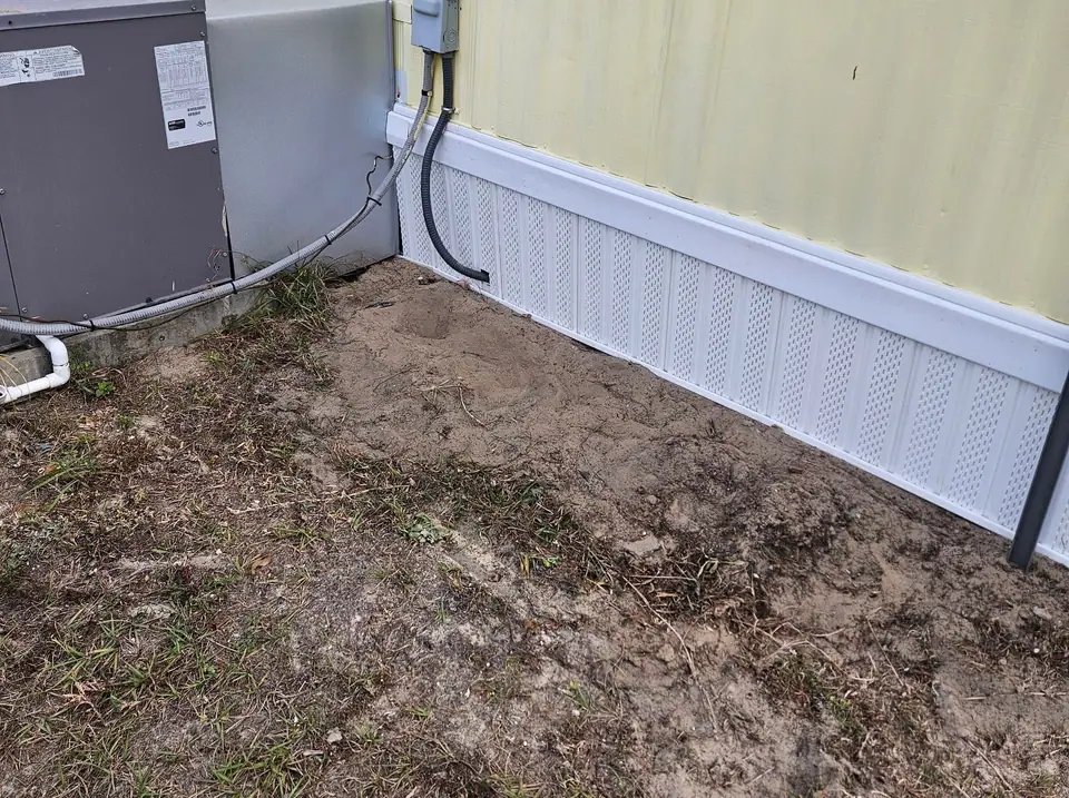 A yellow manufactured home with new white skirting beside the AC unit
